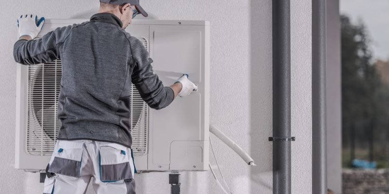 Heat Pump Replacing by Professional Caucasian Heating Technician. Industrial Theme.